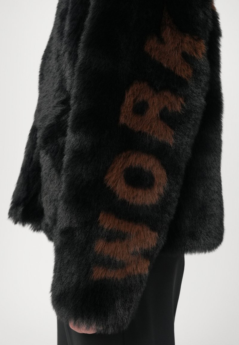 Zwarte nepbontjack met een bruine "WORK" tekstdetail, met een zachte textuur en een ronde silhoutte.