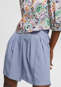 Jasnoniebieskie plisowane spodenki o gładkiej fakturze z bocznymi kieszeniami, połączone z kolorową bluzką w kwiatowy wzór.
