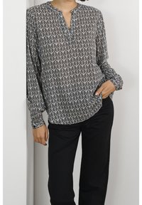 Långärmad blus i svart och vitt lövmönster, med en slagkrage och avslappnad passform, kombinerad med svarta byxor. Mjuk tygkänsla.
