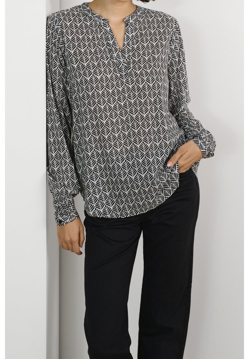 Långärmad blus i svart och vitt lövmönster, med en slagkrage och avslappnad passform, kombinerad med svarta byxor. Mjuk tygkänsla.