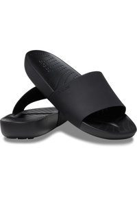 Paire de sandales slides noires Crocs avec une large bride à l'avant et une semelle texturée, empilées en forme de X sur fond blanc.