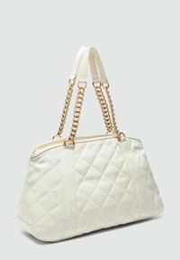 Sac fourre-tout blanc matelassé en simili cuir, avec une poignée en chaîne dorée, un zip sur le dessus et des détails cousus sur la surface.