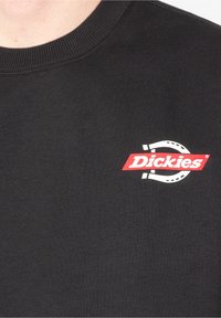 Sweat-shirt noir en tissu mélangé coton avec un col rond. Affiche un logo "Dickies" rouge et blanc avec un graphique de fer à cheval.