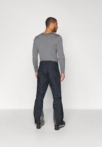 Marineblauwe waterdichte broeken met een relaxte pasvorm, voorzien van ritsen bij de boorden en meerdere zakken, gecombineerd met een grijze langesleeve shirt.