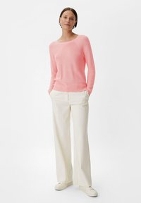 Rosa leichter Strickpullover mit Rundhalsausschnitt, kombiniert mit weißen weiten Hosen und weißen Sneakers, was einen lässigen Look erzeugt.