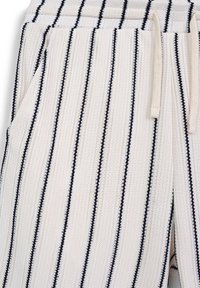 Pantalons lounge en tricot avec une base blanche et des rayures verticales bleues marines, dotés d'un cordon de serrage, de poches latérales et d'un matériau tissé texturé.