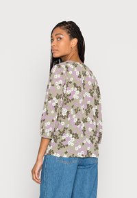 Blusa floral em verde-oliva com mangas bufantes. Apresenta flores roxas, brancas e castanhas. Corte solto e decote redondo, combinada com denim.