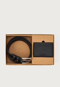 Cinturón de cuero negro con hebilla plateada y tarjetero negro texturizado en una caja de cartón. El tarjetero presenta un detalle en relieve.