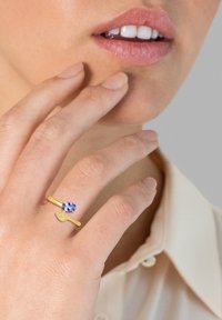 Gouden ring met een ovale blauwe edelsteen en een bladvormig accent. Gladde metalen afwerking met een eenvoudig, elegant ontwerp.
