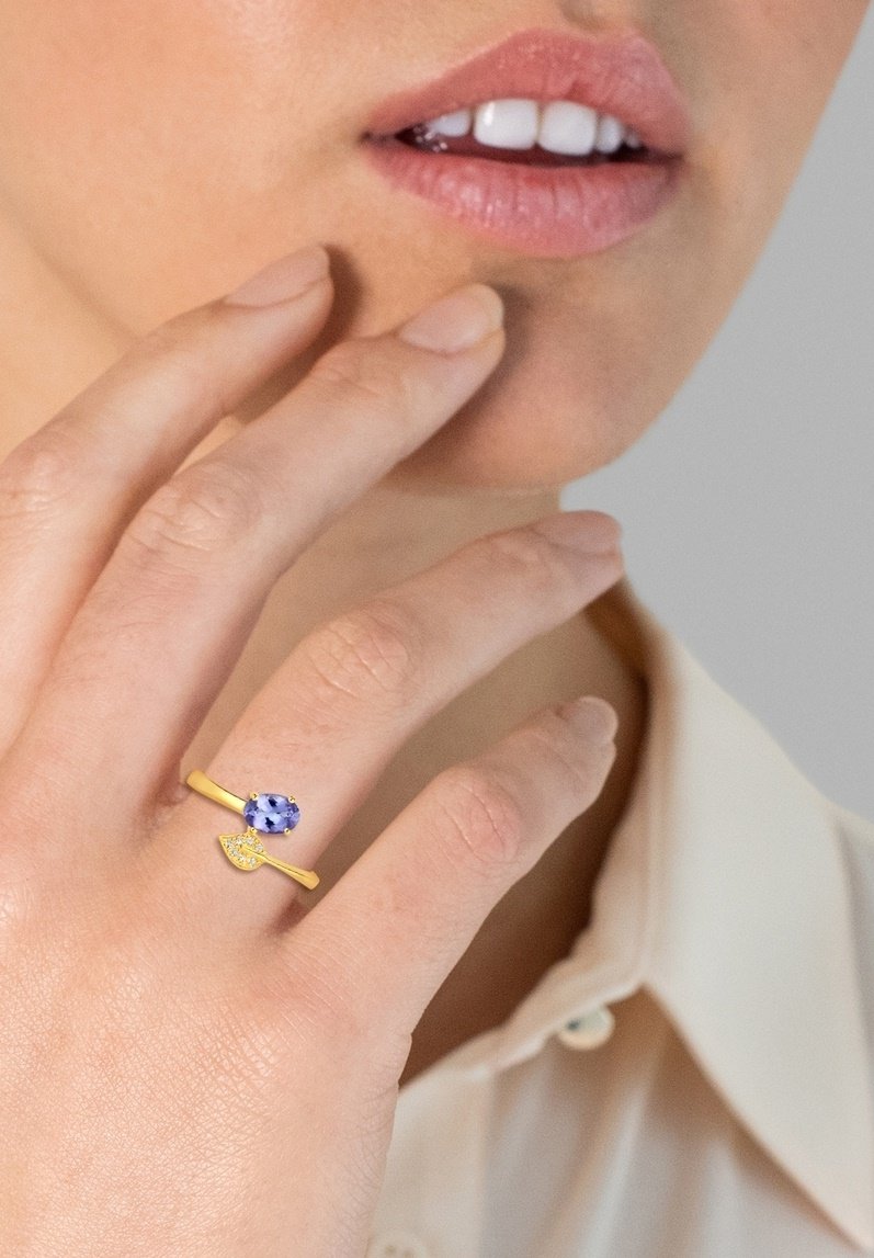 Gouden ring met een ovale blauwe edelsteen en een bladvormig accent. Gladde metalen afwerking met een eenvoudig, elegant ontwerp.