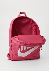 Rosa ryggsäck med en stor framficka som har en vit Nike-logotyp, tillverkad av slitstarkt tyg med en slät textur och en handtag på toppen.