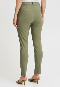 Olivově zelené slim-fit kalhoty s hladkou texturou, poutky na opasek a dvěma zadními kapsami. Doplněné nude sandály s otevřenou špičkou.