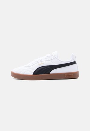 Baskets blanches Puma avec bande latérale noire et semelle marron, vues de profil sur un fond gris clair.