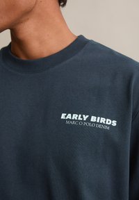 Sweat-shirt à col rond de couleur marine en mélange de coton, avec le texte blanc « EARLY BIRDS MARC O POLO DENIM » en caractères gras sur la poitrine.