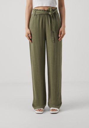 Olive green wide-leg pants with paperbag waist and fabric belt tied in a bow, worn with a white cropped top and white open-toe sandals.