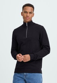 Crni zip-up dukserica s visokim ovratnikom i rebrastim manžetama. Napravljena od mekanog materijala, ima srebrni patentni zatvarač i uski kroj.
