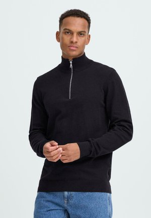 Sweat-shirt noir zippé avec un col haut et des poignets côtelés. Fabriqué en tissu doux, il possède une fermeture éclair en argent et une coupe ajustée.