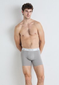 Boxer da uomo grigi realizzati in materiale morbido con un design aderente. Presentano un elastico bianco in vita con il logo "Calvin Klein".
