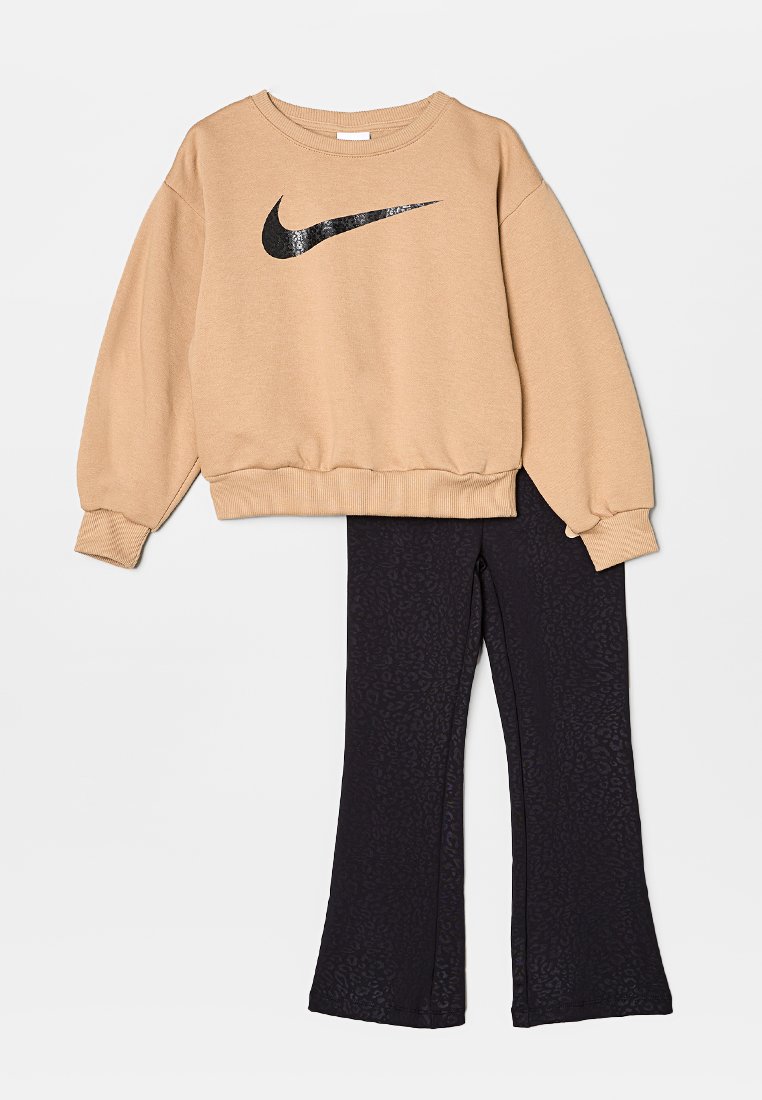 Sudadera beige de Nike con un logo de lentejuelas negras, combinada con leggings negros de pierna acampanada que presentan una sutil textura de estampado animal.