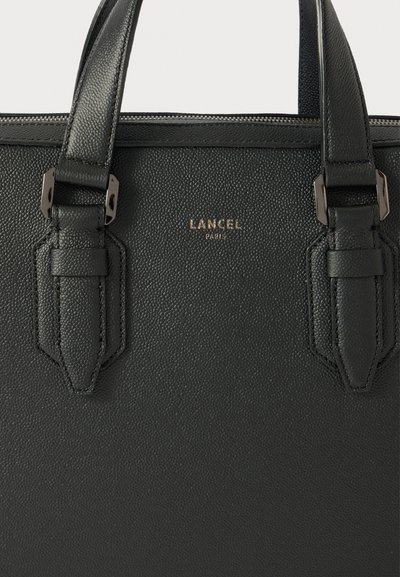 Sac à main en cuir texturé noir avec deux anses supérieures, comportant des accents en métal et un logo doré en relief à l'avant.