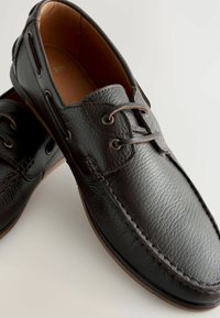 Pantofi din piele neagră cu suprafață texturată, vârf rotund, accente maro și șireturi. Talpă din cauciuc și detalii de cusătură pe laterale.