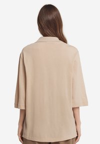 Beige, losse shirt met kraag en 3/4 lengte mouwen, gemaakt van een zacht materiaal, met een gladde textuur en rechte zoom.