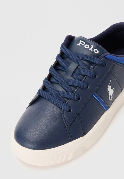 Sapatilha de couro azul-marinho com superfície texturizada, sola de borracha branca, atacadores alinhados e detalhe do logo. Apresenta uma faixa contrastante azul.