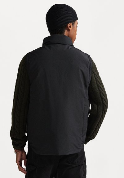 Black, sleeveless vest with a high collar, paired with a dark green, textured, cable-knit sweater. Features a smooth, matte exterior.