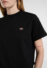 Must black t-särk, millel on ümar kaelus ja lühikesed varrukad. Vasakul rinnal on nähtav väike logopatch.