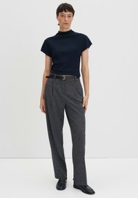 Haut bleu marine à côtes avec un col montant, associé à un pantalon large en tissu texturé gris et une ceinture noire. Le modèle porte des chaussures noires.