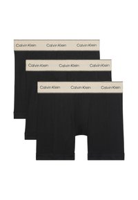 Tre svarta Calvin Klein boxershorts med beige elastiska midjeband som har upprepade Calvin Klein-logotyper.