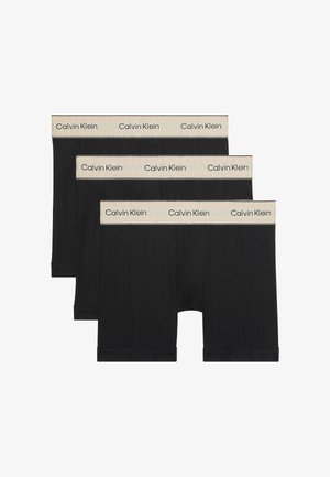 Tre paia di boxer neri Calvin Klein con cinturini elasticizzati beige che presentano il logo Calvin Klein ripetuto.