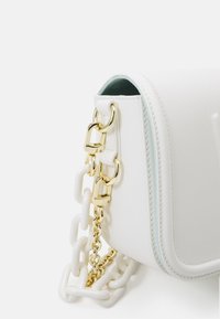 Vägg i vitt läderhandtag med guldaccessoarer och en axelrem som kombinerar stora vita länkar och fina guldkedjelänkar.