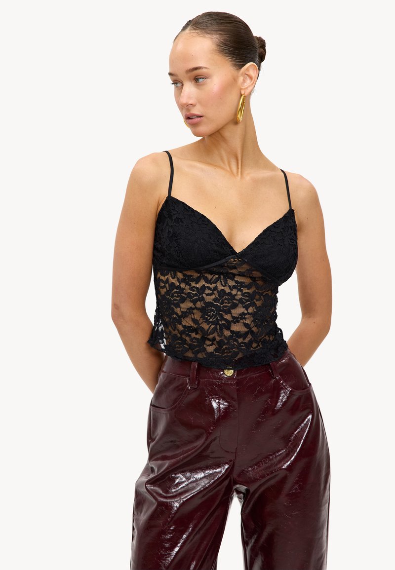 Zwarte kanten camisole met dunne bandjes en een bloemenpatroon, gecombineerd met glanzende bordeauxrode high-waisted broek. Textuurdetail op de stof.