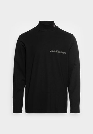 Czarna koszulka z długim rękawem i golfem z napisem "Calvin Klein Jeans" na piersi i małym logo na kołnierzu.