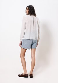 Leichte, transparente weiße Bluse mit vertikalen Streifen; kombiniert mit hellblauen Jeansshorts. Braune Lederloafers runden das Outfit ab.