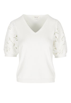 Valge lühikeste varrukatega silmuskootud top V-kaelusega ja läbipaistvate lillelise pitsiga täispuhutud varrukatega, liibuv sääris ning väikese brändi sildiga kaeluse sees.