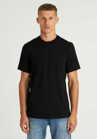 Crna pamukasta majica s kratkim rukavima, kružnim izrezom i malim logotipom na prsima. Glatka tekstura i prilagođeni dizajn.