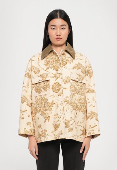 Beige takki, jossa on kukkakuosi ja teksturoitu pinta, ruskea corduroytakakääntö ja kaksi etutaskua. Rentomallinen ja pitkät hihat.