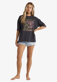 Sort oversized t-shirt med et farverigt palmetræsgrafik, parret med slidte lyseblå denimshorts. Korte ærmer, afslappet pasform.