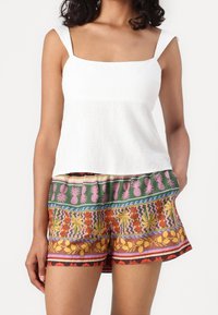 Biała lniana bluzka z kwadratowym dekoltem i ramiączkami, zestawiona z żywymi szortami w wielobarwny wzór owoców i kwiatów.