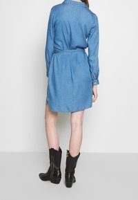 Denim-mekko, vaaleansininen, pitkät hihat, vyö vyötäröllä, puolivälin reisiin saakka, takana poimutukset, yhdistetty mustiin nilkkabotteihin.