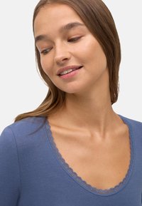 Blusa azul con escote redondeado, que presenta un delicado borde de encaje. Tejido suave y liso con una forma ajustada y mangas largas.