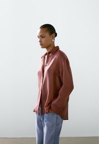 Løs siddende, rustfarvet skjorte med knaplukning i front, lange ærmer og en blød tekstur. Kombineret med lyseblå denimjeans.