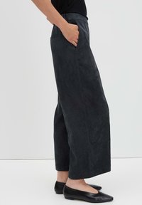 Pantaloni in velluto a coste grigio scuro con una vestibilità rilassata, dotati di tasche laterali e una superficie testurizzata. Vita liscia, senza hardware visibile.