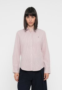 Chemise boutonnée à rayures rouges et blanches avec un col classique, des manches longues et un petit logo sur la poitrine. Texture de tissu lisse.