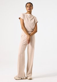 Top beige de punto con escote drapeado y mangas cortas, combinado con pantalones de pierna ancha de talle alto a juego y zapatillas beige gruesas.