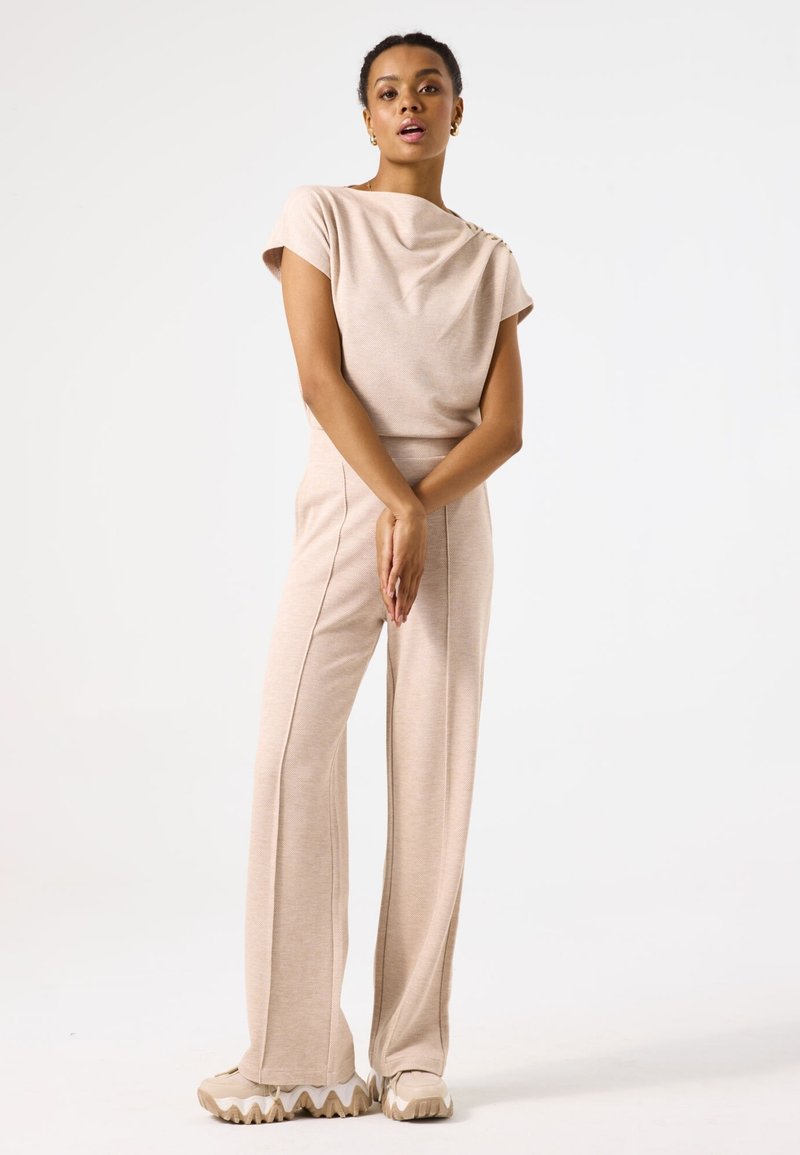 Top beige de punto con escote drapeado y mangas cortas, combinado con pantalones de pierna ancha de talle alto a juego y zapatillas beige gruesas.