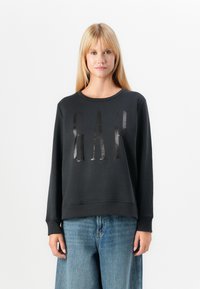 Black sweatshirt with a round neckline and long sleeves, featuring a glossy "GAP" logo on the front. Paired with light blue wide-leg jeans.