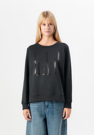 Black sweatshirt with a round neckline and long sleeves, featuring a glossy "GAP" logo on the front. Paired with light blue wide-leg jeans.